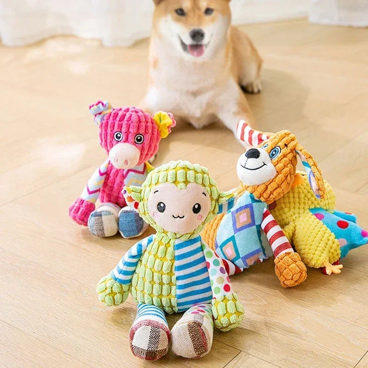 Pets-Shop Colorful plush toys in the shape of a giraffe, sheep, and dog in front of a real dog on a wooden floor. Shopets-Amazon.